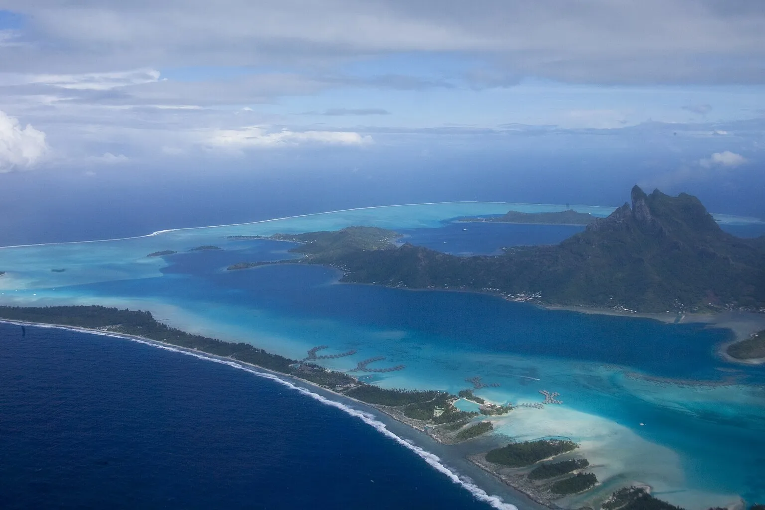 Vue aérienne de Bora-Bora : lagon turquoise, récif-barrière, bungalows sur pilotis et mont Otemanu
